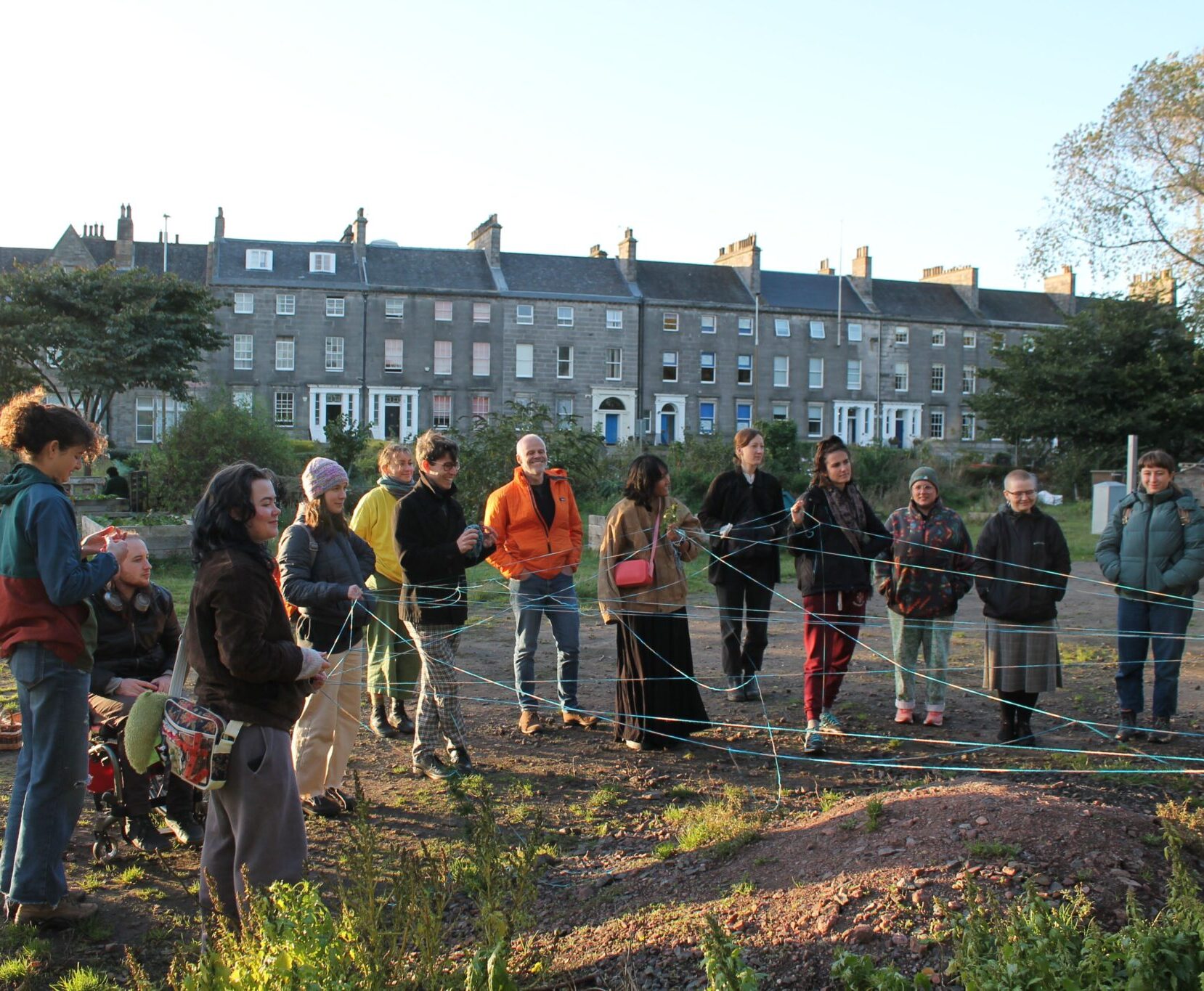 A group of adults in a circle outdoors, with their hands connected by string.