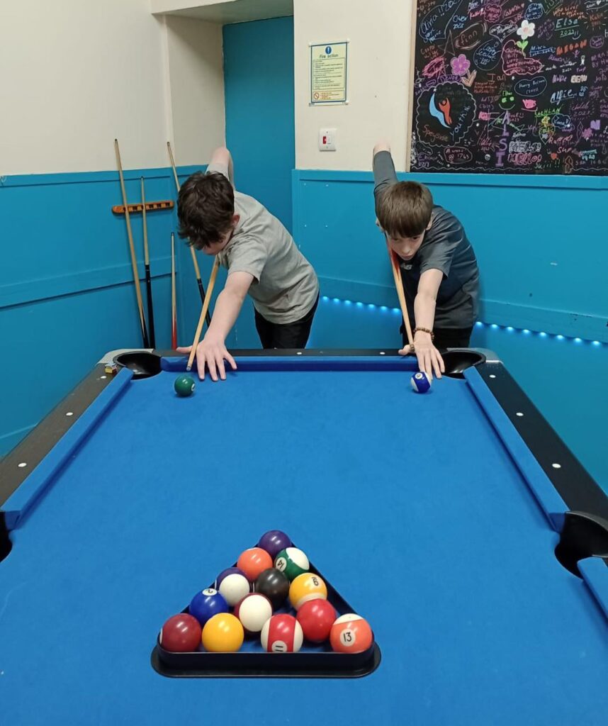 Two young people holding a cue over a pool table.