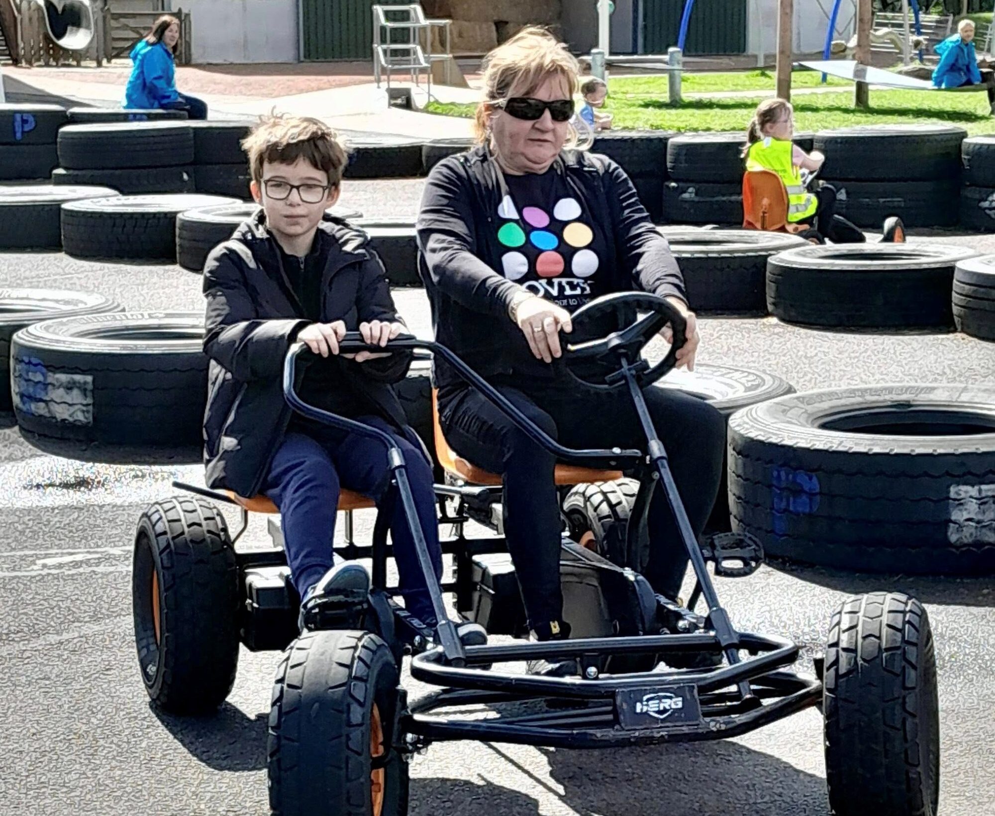 An adult and young person on a go kart going around a track.
