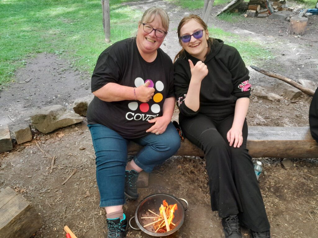Two people sitting on a log by a small campfire.