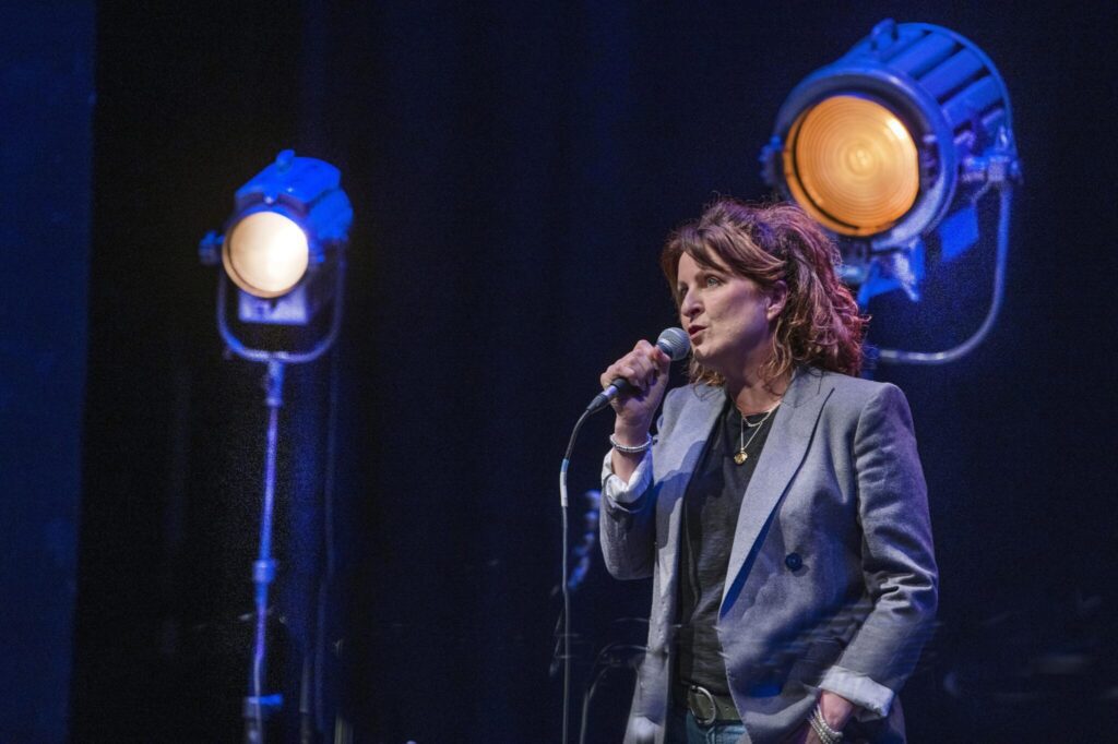 Person standing with a microphone on a stage with lights.