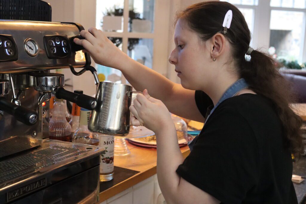 Young person making hot milk using a professional coffee machine.
