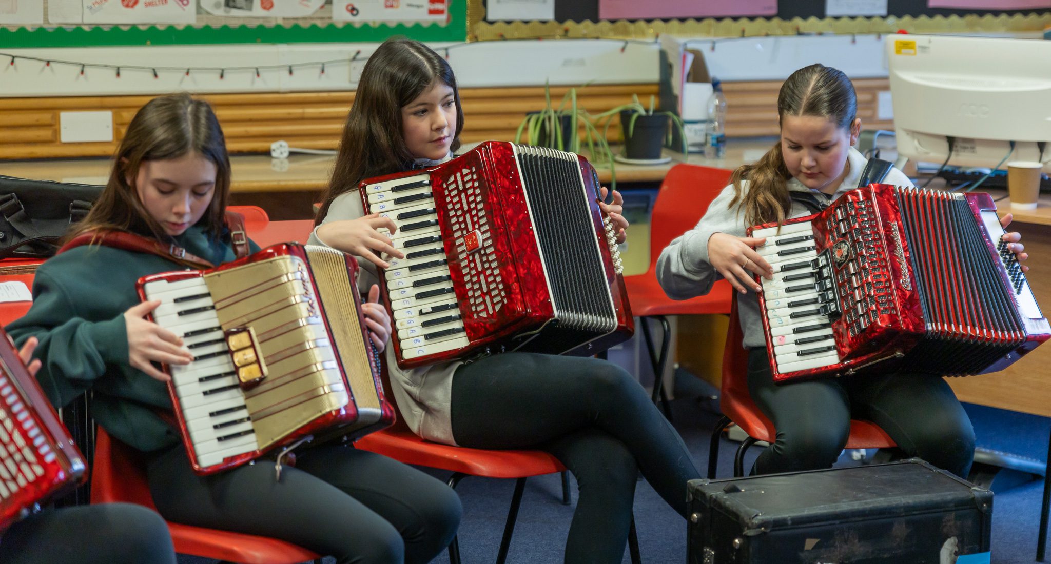 Three young people sitting on seats and playing accordian musical instruments.