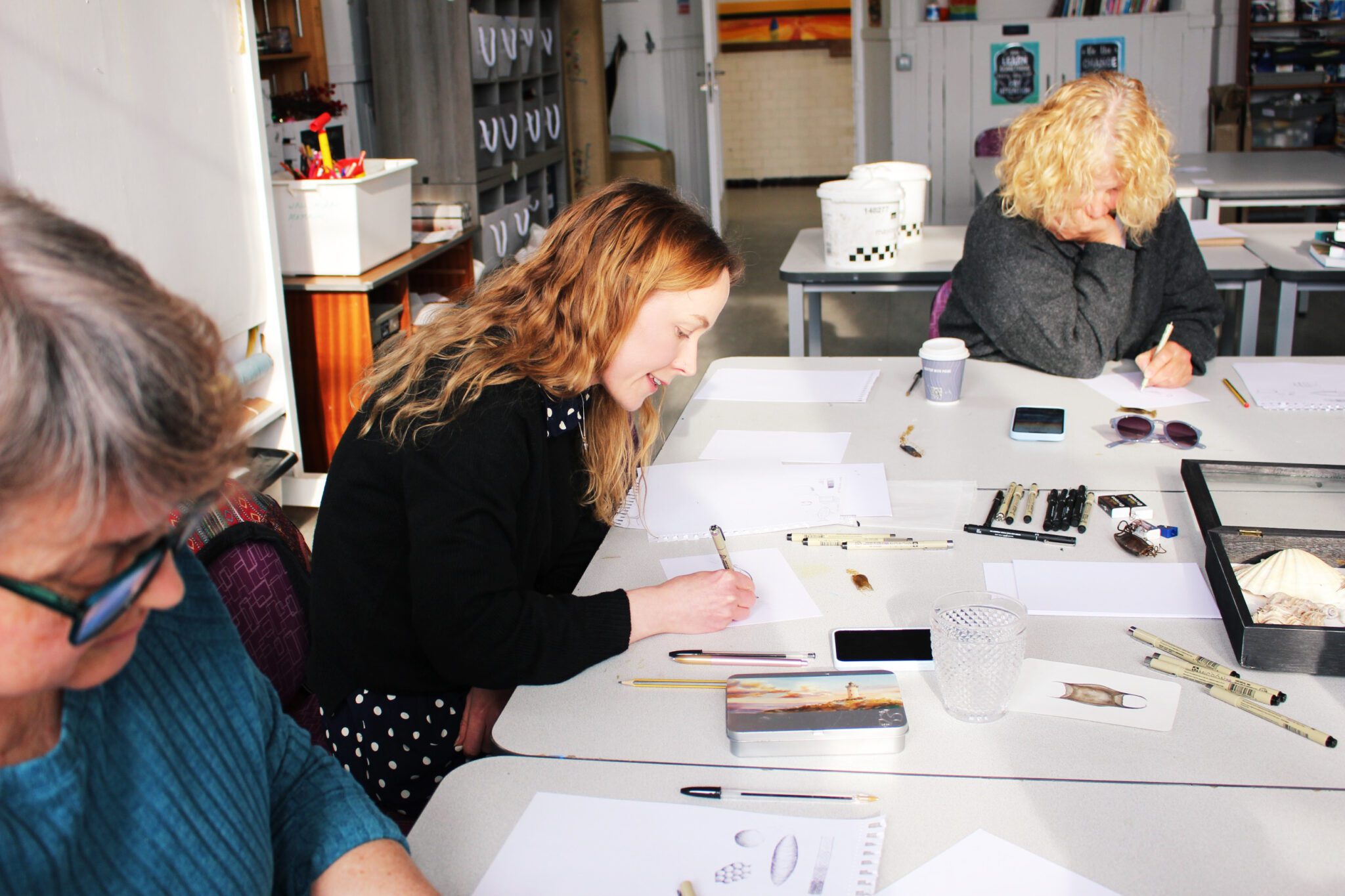 Three people sitting around large desks and drawing on paper.
