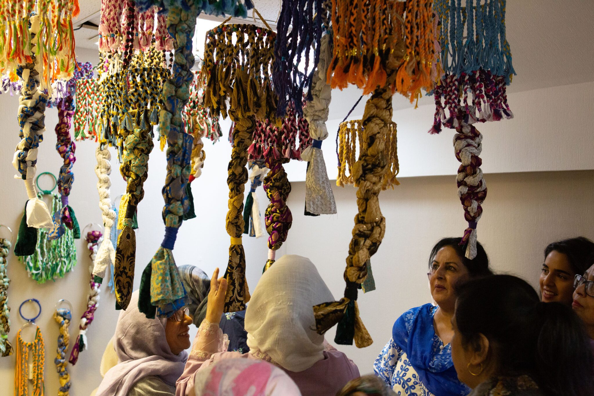 A group of women walking through an art installation of hanging colourful fabric.