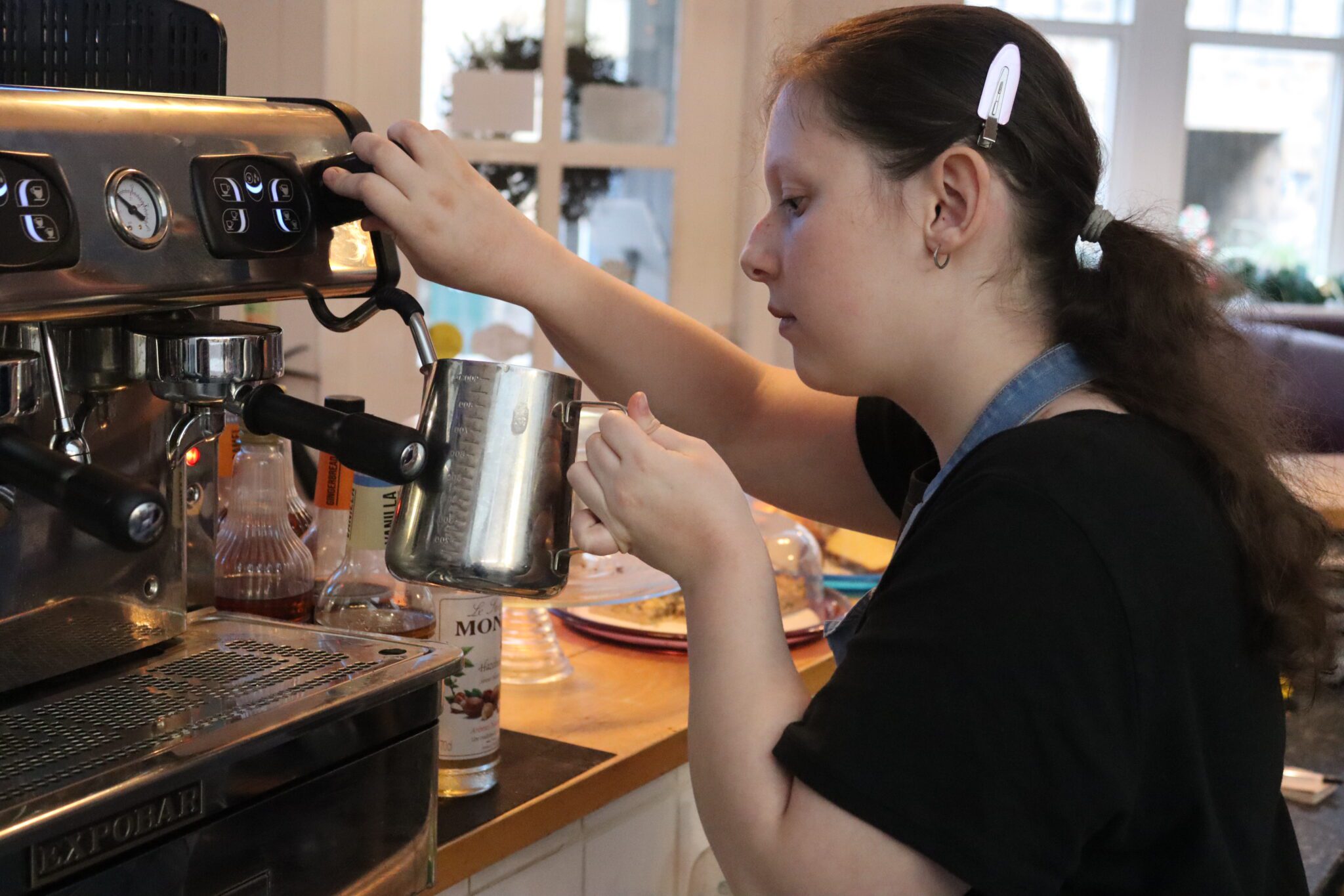 Young person making hot milk using a professional coffee machine.