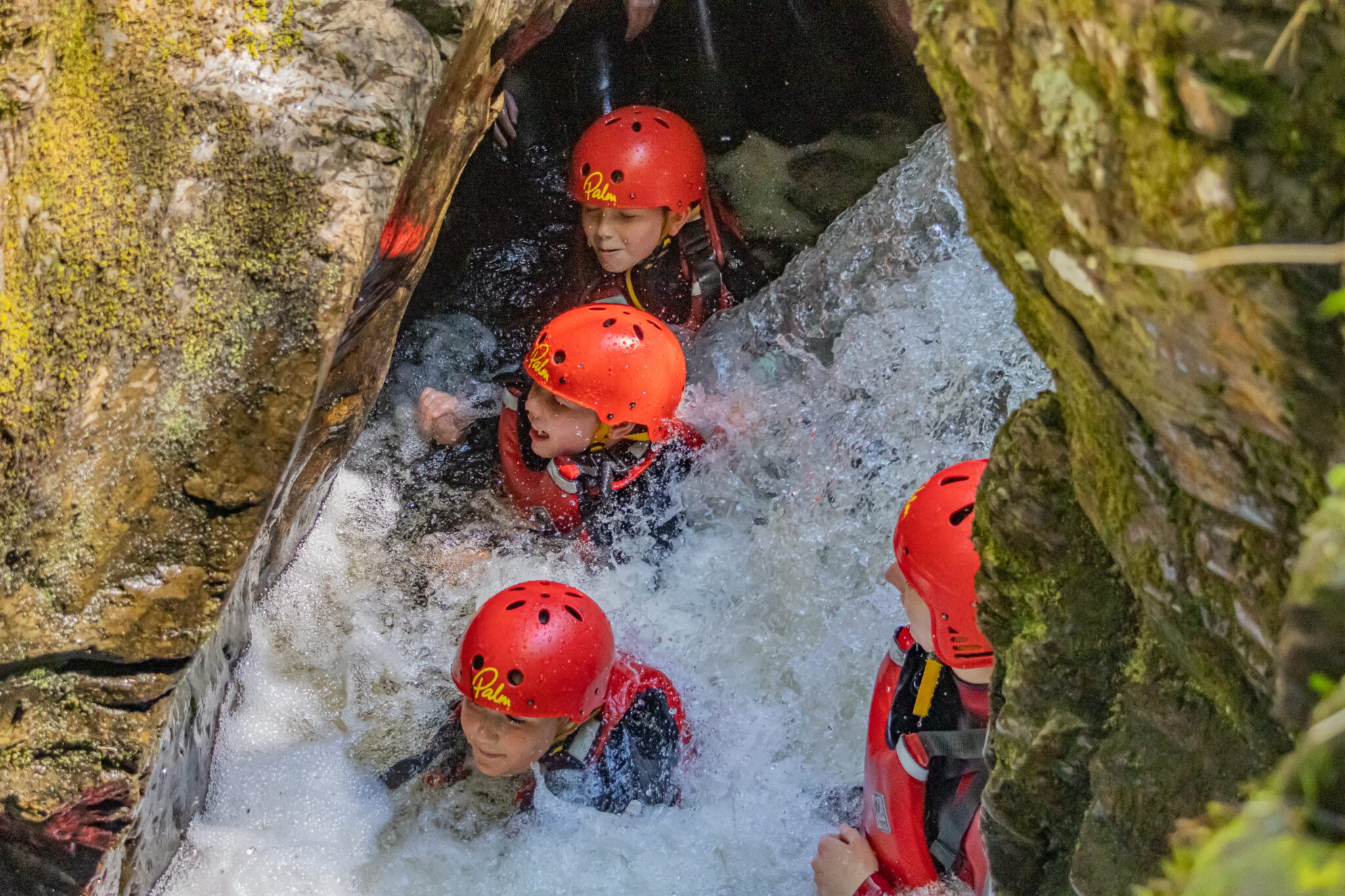 Four young people doing outdoor pursuits in fast water and wearing red helmets.